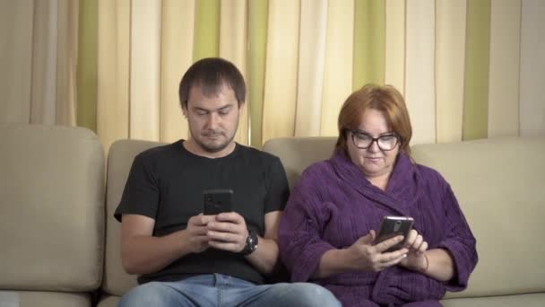 Man and woman ignore each other on the sofa while using their smartphones for social media. — Stock Video