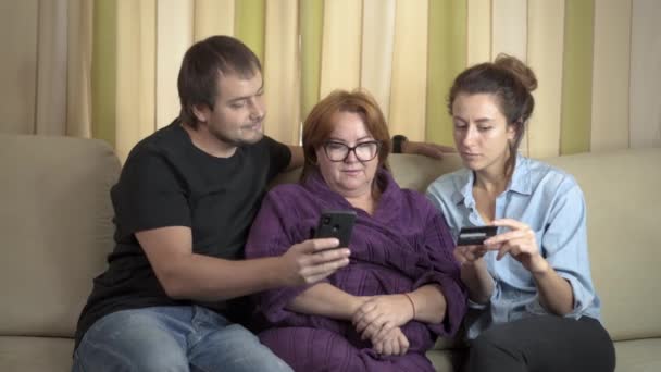 Mãe sênior e sua filha e filho usando tablet em casa. Compras com cartão de crédito no celular. Adolescente neta ensinando avó como usar celular e fazer compras on-line — Vídeo de Stock