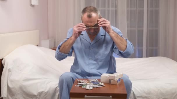 Gammal man sitter i pyjamas på säng med piller i skål på Nattduksbord, deprimerad — Stockvideo