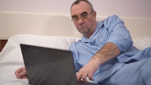 Ανώτερος άνθρωπος χρησιμοποιώντας το laptop στο κρεβάτι στο υπνοδωμάτιο στο σπίτι 4k — Αρχείο Βίντεο