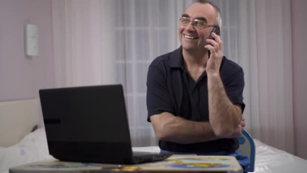 Пожилой человек за компьютером разговаривает по телефону, эмоции радости и счастья — стоковое видео
