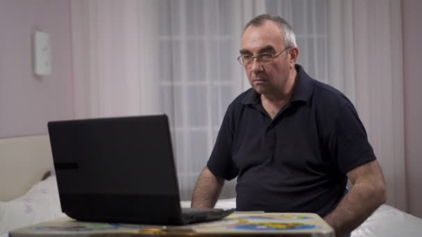Anciano de pelo gris masculino usando el ordenador portátil, viendo el fútbol en un ordenador portátil y se regocija — Vídeos de Stock
