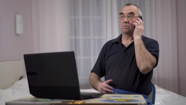 Een oudere man op de computer praten over de telefoon, emoties van verrassing — Stockvideo