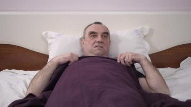 Yaşlı bir adam yatakta dinlenirken yatıyor. Uzaklaşmasını engelleyen sinekler ve sivrisinekler uzakta sürücüler