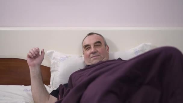 En äldre man ligger i sängen vilar, känsla av lycka, glädje, tröst — Stockvideo