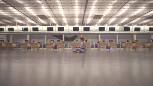 Mädchen sitzt im Terminal auf dem Boden des Flughafens arbeitet mit einem Laptop während des Wartens auf den Flug. — Stockvideo