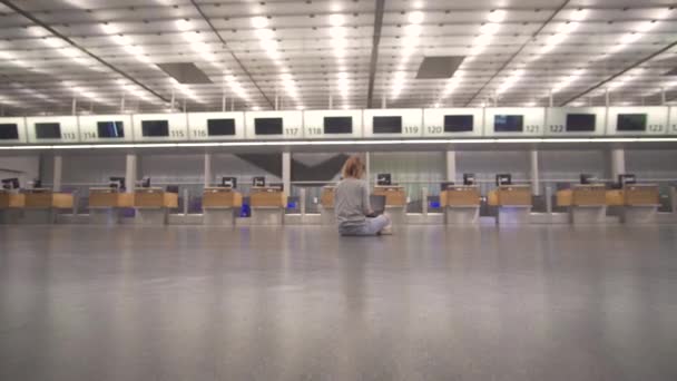 Menina senta-se no terminal no chão do aeroporto trabalha com um laptop enquanto espera o voo . — Vídeo de Stock