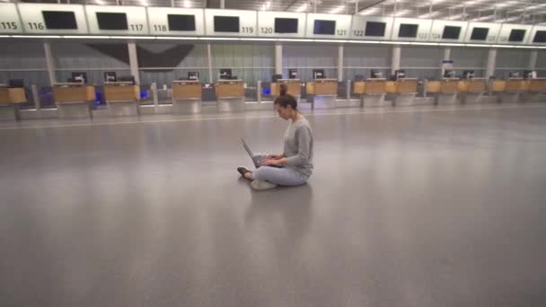 女性はラップトップで作業し、床の上のターミナルで空港でのフライトを待っています. — ストック動画
