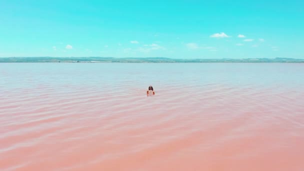 Havadan görünüm. Güzel bir genç kız pembe göl, bir bikini, güneş gözlüğü, pembe berrak su, bir üst görünümü yatıyor. Konsept: deniz havası, yaz, seyahat, tatil, özgürlük, güneş, zevk — Stok video