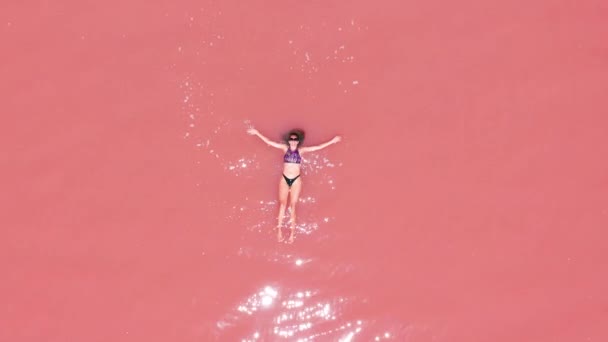 Pembe tuz gölünde yüzen bikinili çekici bir kadının havadan görünümü. — Stok video