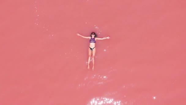 분홍색 소금 호수에 떠있는 비키니를 입은 매력적인 여성의 공중 보기. — 비디오