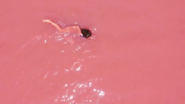 Vista aérea de una atractiva mujer en bikini flotando en un lago de sal rosa . — Vídeos de Stock