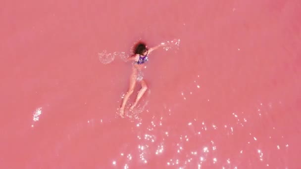 Vista aerea. Una bella ragazza si trova nel lago rosa, un bikini, occhiali da sole, acqua limpida rosa, una vista dall'alto. Concetto: aria di mare, estate, viaggi, vacanze, libertà, sole, godere — Video Stock