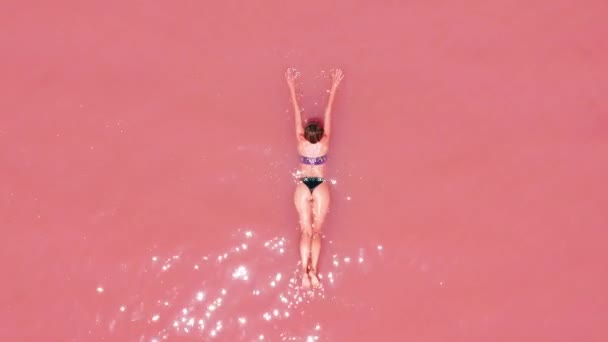 Flygvy. En vacker ung flicka ligger på i rosa sjön, en bikini, solglasögon, rosa klart vatten, en topputsikt. Koncept: havsluft, sommar, resa, semester, frihet, sol, Njut — Stockvideo