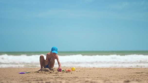Un bambino sta giocando nella sabbia sul mare, gambe e dita piccole, uno sfondo di sabbia gialla di mare e acqua blu. Concetto: bambini, infanzia, estate, libertà, bambini, bambino . — Video Stock