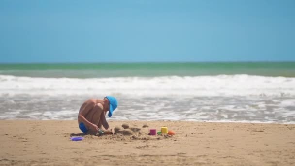 Маленький хлопчик грає на піску на морі, маленьких ногах і пальцях, на фоні морського жовтого піску і блакитної води. Концепція: діти, дитинство, літо, свобода, діти, дитина . — стокове відео