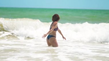 Young happy woman run into the sea with lot of splashes and jump over the breaking wave.
