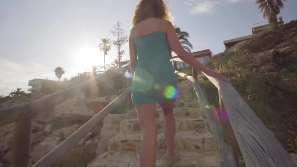 Vue de derrière. Une jeune femme sort de la plage en montant les escaliers. Une femme monte les escaliers dans l'après-midi . — Video