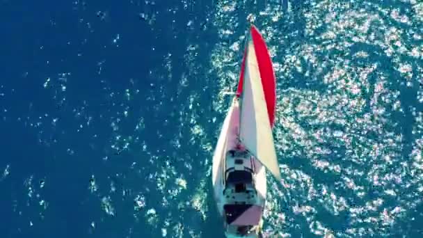 Luchtfoto. Prachtig zeiljacht met een rood zeil is zeilen op de smaragd groene zee op een zonnige dag. — Stockvideo