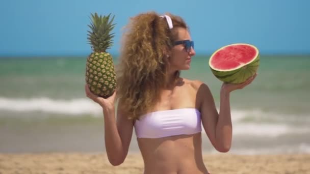 Jovem menina bonita se diverte na praia perto do mar dançando com frutas tropicais. alegria conceito e comida saudável . — Vídeo de Stock