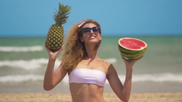 Joven hermosa chica se divierte en la playa cerca del mar bailando con frutas tropicales. concepto alegría y comida saludable . — Vídeos de Stock