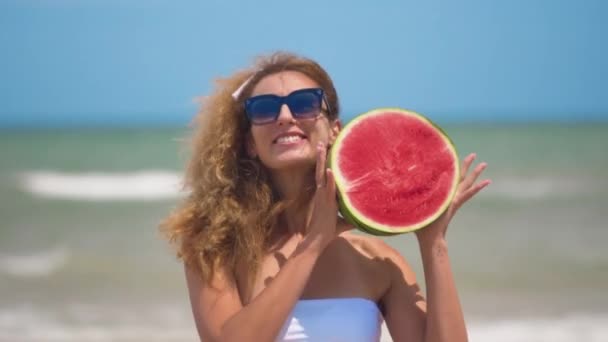 Menina dançando com uma meia melancia suculenta no fundo de um belo mar. Fechar . — Vídeo de Stock