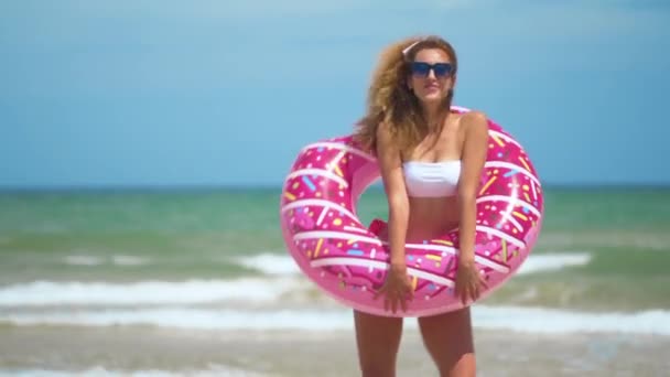 Kvinna som har roligt och leende dansar med rosa munk. flicka i bicini bär solglasögon på stranden. Vacker sexig kvinna på sommarresa semester. — Stockvideo