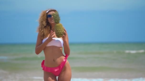 Śmieszne uśmiechnięta dziewczyna w letnich strojów kąpielowych i okulary przeciwsłoneczne. Seksowna kobieta z świeżym ananasem. Pozytywny taniec w pobliżu pięknego morza. — Wideo stockowe