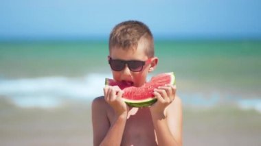 Siyah gözlüklü çocuk denizde karpuz yiyor.