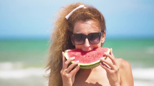 Mujer sonriente comiendo sandía en la playa. Mujer comiendo sabrosas frutas de verano. Feliz verano. . — Vídeos de Stock