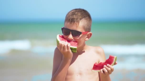 Boy in black glasses eats watermelon on the sea. — Stock Video