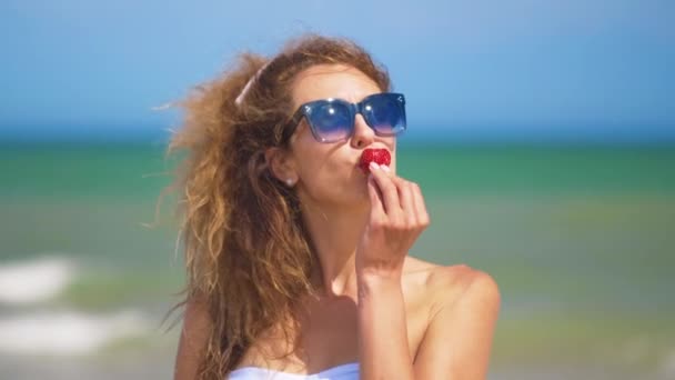 Жінка їсть полуницю біля моря в сонячний літній день . — стокове відео