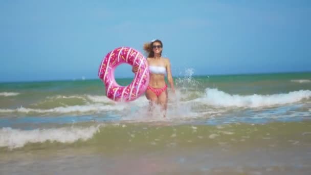 おもちゃで楽しいを持っている若い女性インフレータブルリングドーナツオンザビーチ. — ストック動画
