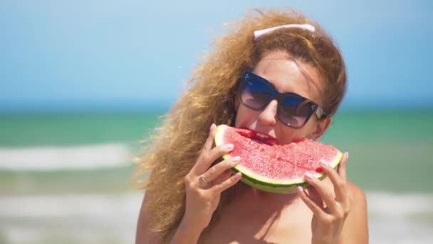 Mujer sonriente comiendo sandía en la playa. Mujer comiendo sabrosas frutas de verano. Feliz verano. . — Vídeo de stock
