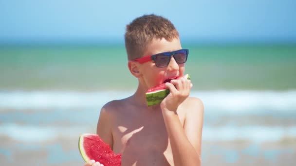 Menino de óculos pretos come melancia no mar . — Vídeo de Stock