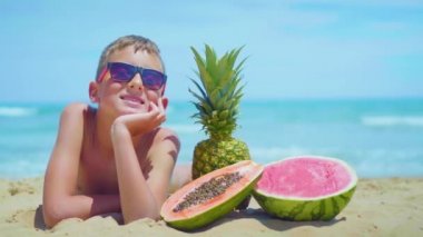 gülümseyen çocuk denize karşı egzotik meyve bir kompozisyon ile deniz kıyısında yatıyor.