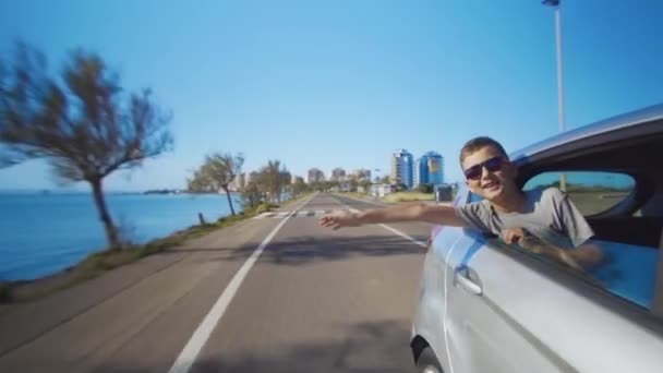 Ragazzo guardando fuori dal finestrino della macchina e agitando la mano . — Video Stock