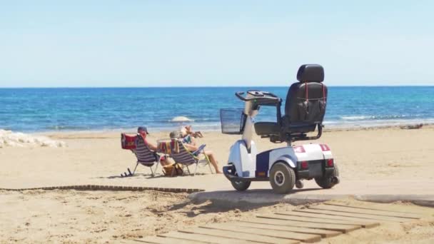 Elektro-Rollstuhl am Strand hinter dem Meer. — Stockvideo