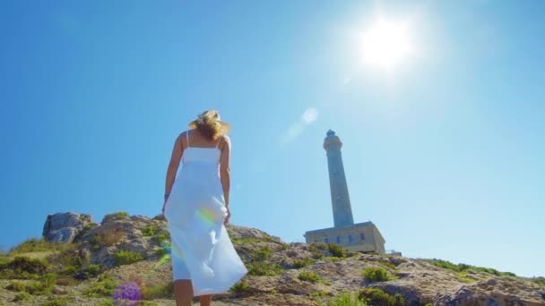 Ein schönes junges Mädchen, blickt auf einen Leuchtturm, mit Strohhut. Konzept: Erholung, schöne Aussicht, Freiheit, Reisen und Atmen. — Stockvideo