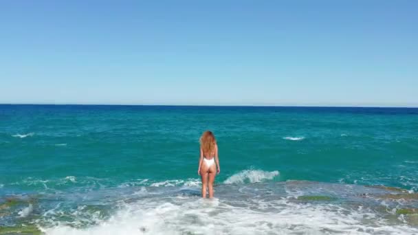 Młoda kobieta w bikini na brzegu morza i rozpryskiwania fale wodne anteny krajobrazu. Piękna kobieta na skalistym morzu plaża Drone widok. — Wideo stockowe