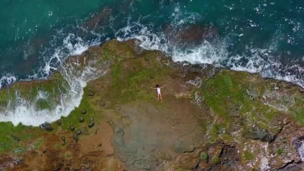 Letecký pohled. Mořské vlny se stříkající pěnou a sprejem na kamenné pobřeží. Krásná žena leží na skalnaté pláži. — Stock video