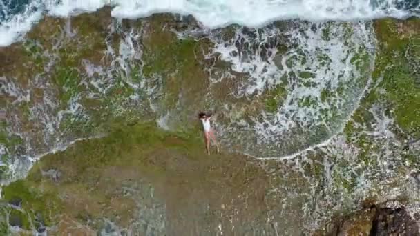 Letecký pohled. Mořské vlny se stříkající pěnou a sprejem na kamenné pobřeží. Krásná žena leží na skalnaté pláži. — Stock video