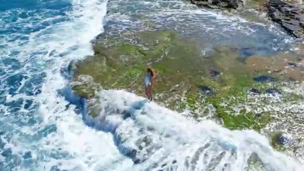 Vista aerea. Ragazza sexy in piedi sulla scogliera sulla spiaggia rocciosa. Una donna guarda lontano. . — Video Stock