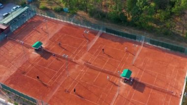 Güneşli bir yaz gününde turuncu kortta tenis oynayan tanınmayan tenisçilerin havadan üst görünümü.
