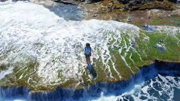 Vista aérea. Sexy Girl de pie en el acantilado en la playa rocosa. Una mujer mira a la distancia . — Vídeos de Stock