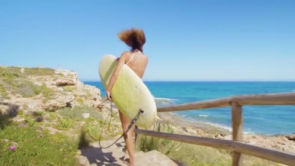 Vista posteriore della ragazza surfista attraente, a piedi sulla spiaggia con tavola da surf . — Video Stock