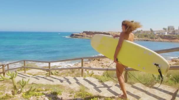 서핑 보드와 함께 해변을 따라 걷는 무두질 한 피부를 가진 섹시한 소녀. 비키니 수영복을 입은 아름다운 젊은 여성. 피트니스 건강 액티브 리빙의 개념. — 비디오