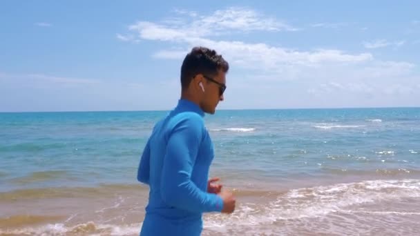 Athletic guy jogging along coast on a sunny day. Jogging outdoor near the sea. Concept healthy, active lifestyle. — Stock Video