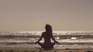 Gün batımında plajda kız pratik yoga. Genç kız tropikal bir plajda egzersiz yapıyor. Bir plajda bir kadın Yoga silüeti.