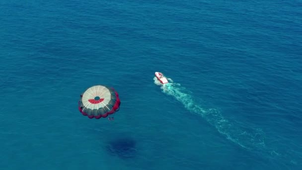 Havadan görünüm. Renkli bir paraşütle uçan insanlar motorlu bir tekne tarafından çekilsinler. Mavi gökyüzünde parasailing. — Stok video